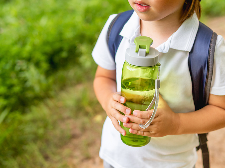 Grade school student wearing book bag and holding water bottle.